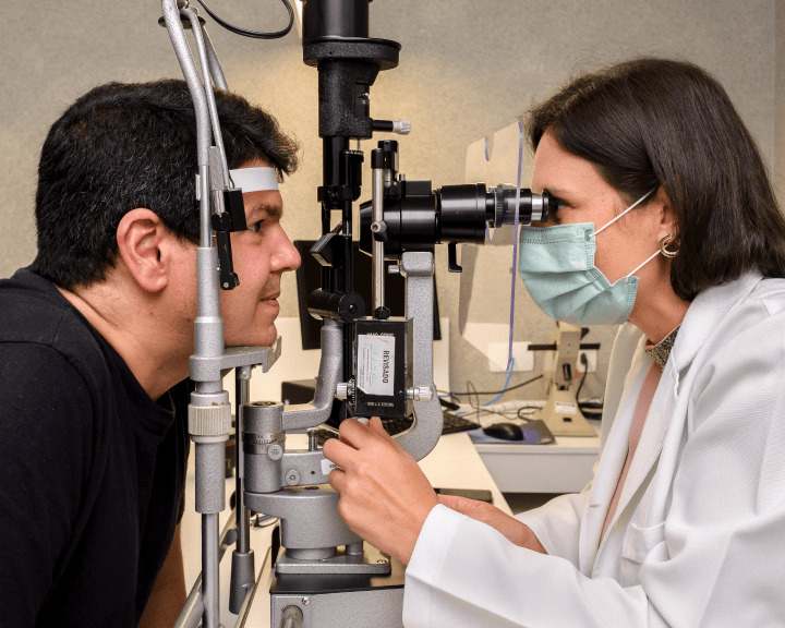 Oftalmologista mulher examinando os olhos de uma paciente homem por meio de um aparelho. Representação da especialidade oftalmologia.